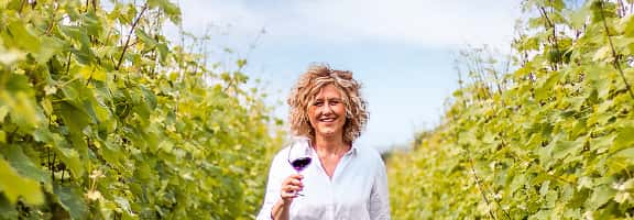 Donna sorridente tra i filari con un calice di vino – vigneto di Turbiana nel territorio del Lugana