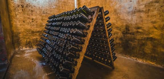 Wine Bottles in Stone Cellar  Bottiglie di spumante in affinamento su pupitre in cantina – lavorazione tradizionale di vini premiati