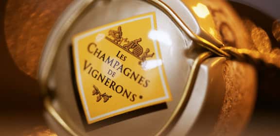 Tappo di una bottiglia di Champagne con etichetta 'Les Champagnes de Vignerons', simbolo dell’eccellenza artigianale francese