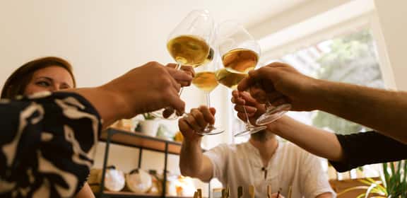 Brindisi con calici di vino bianco tra amici, ideale per l’aperitivo.