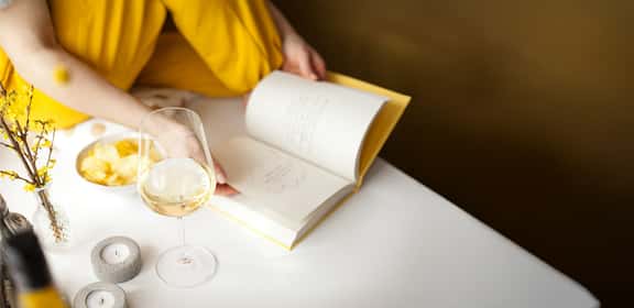 Calice di vino bianco mentre si sfoglia un libro, momento di relax con Travino