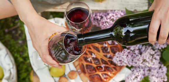 Versare vino dolce rosso in un bicchiere durante un picnic, dettagli floreali sullo sfondo.